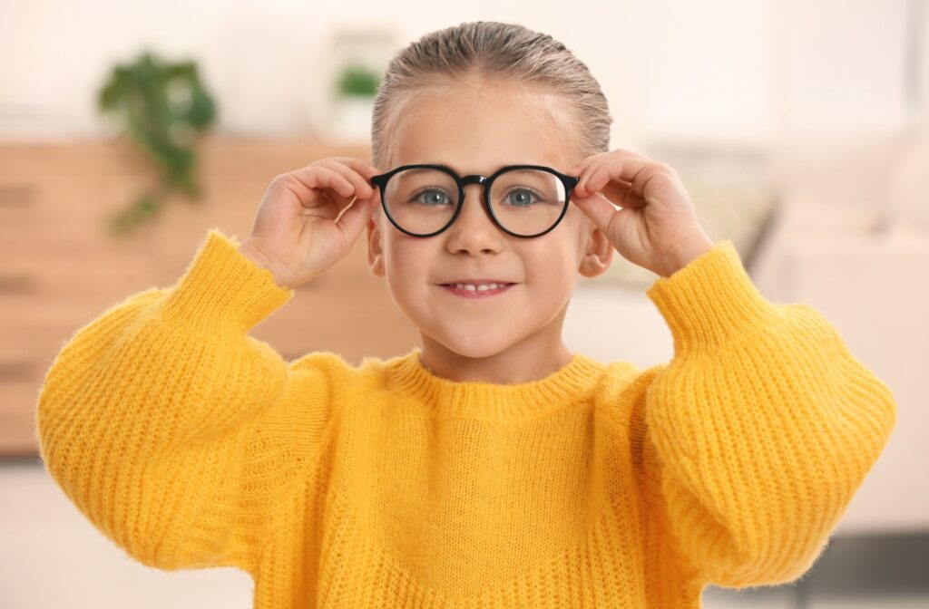 A young child wearing a yellow sweater holds their glasses up to their face