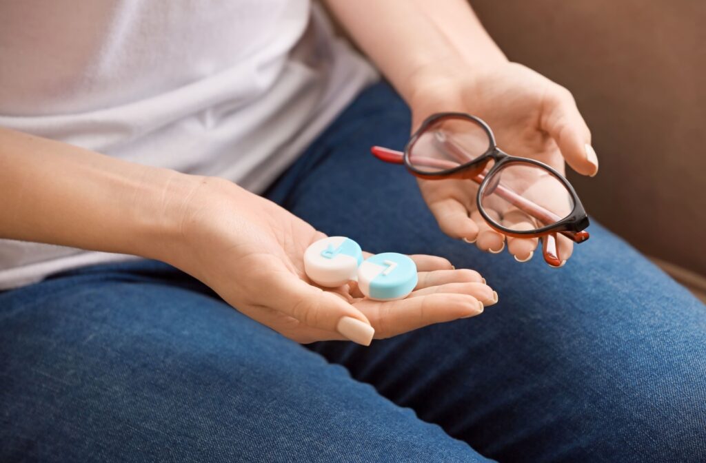 A person holding a pair of glasses in one hand and a pair of contact lenses in the other hand